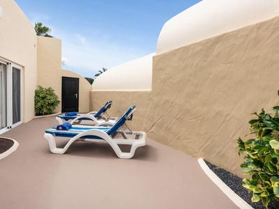 Zwei blaue Liegestühle auf einer Terrasse mit beigem Boden vor beigen Wänden unter blauem Himmel.