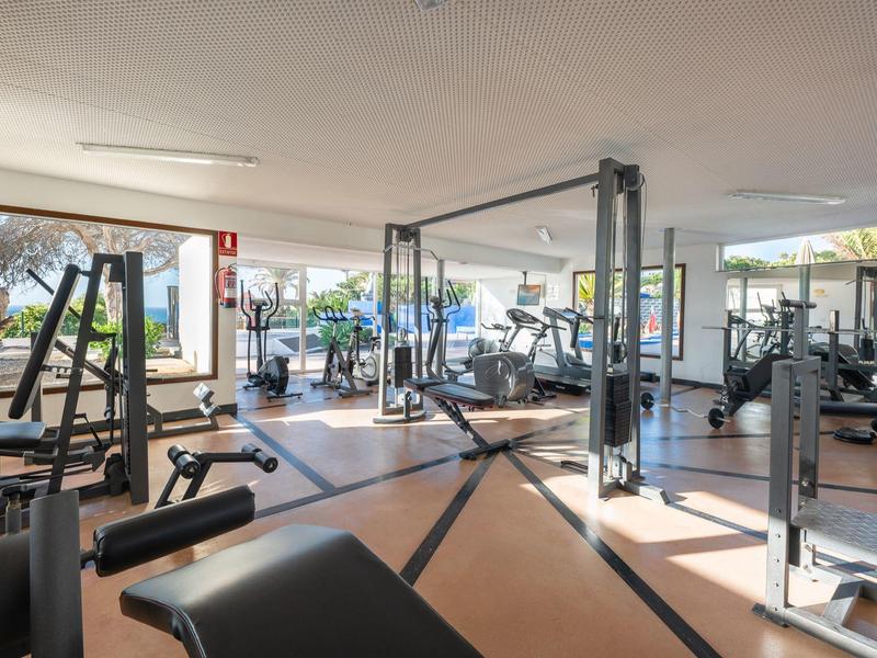 Großer Fitnessraum mit modernen Geräten und Blick auf den Garten und das Meer.