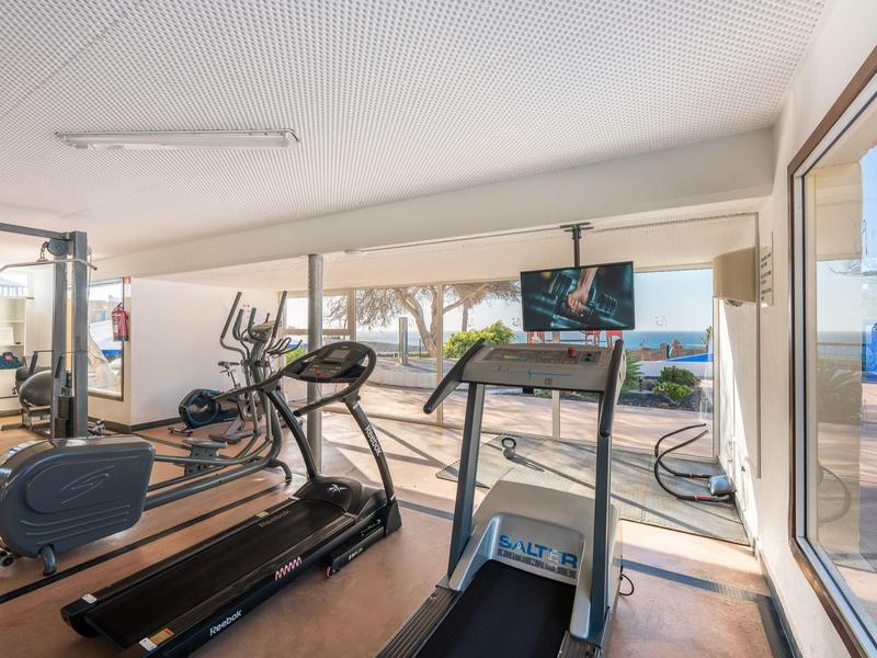 Fitnessraum mit Laufbändern, Crosstrainern und großen Fenstern mit Blick nach draußen.