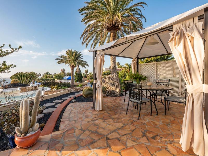 Terrasse mit Pavillon, Tischen, Stühlen und Pflanzen bei Sonnenschein in einem Hotelgarten.