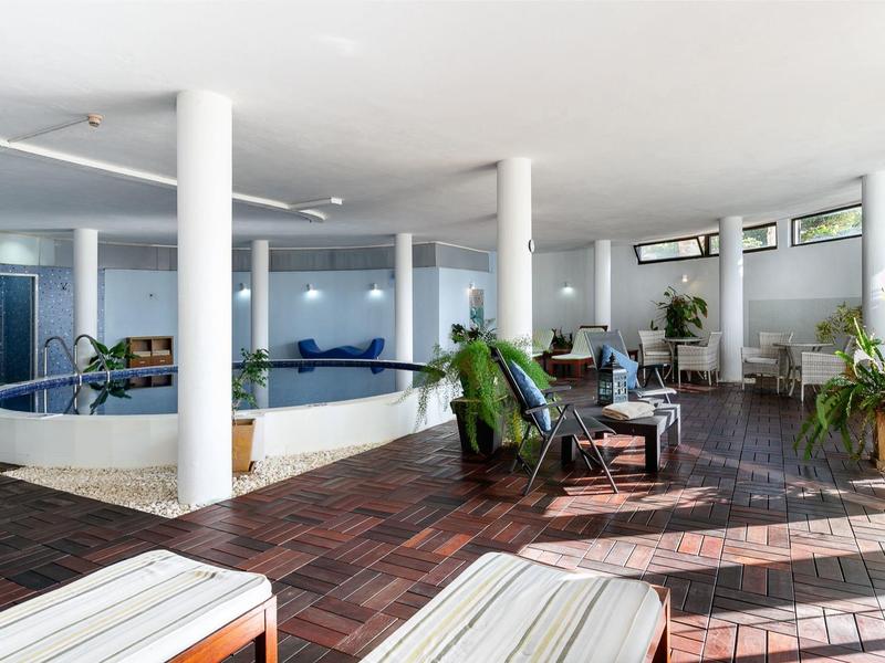 Innenansicht eines ruhigen Wellnessbereichs mit Pool, Liegestühlen und Pflanzen.