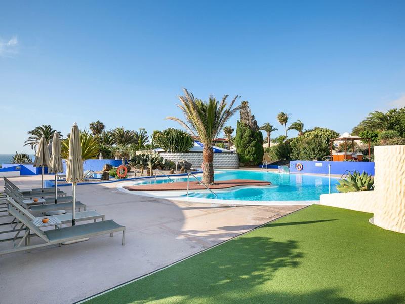 Moderner Hotelpoolbereich mit Sonnenliegen, Palmen und klarem blauem Himmel.