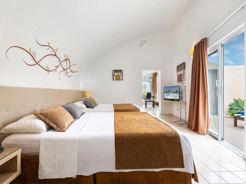 Helles Hotelzimmer mit Doppelbett, braunen Akzenten und Balkon mit Blick nach draußen.