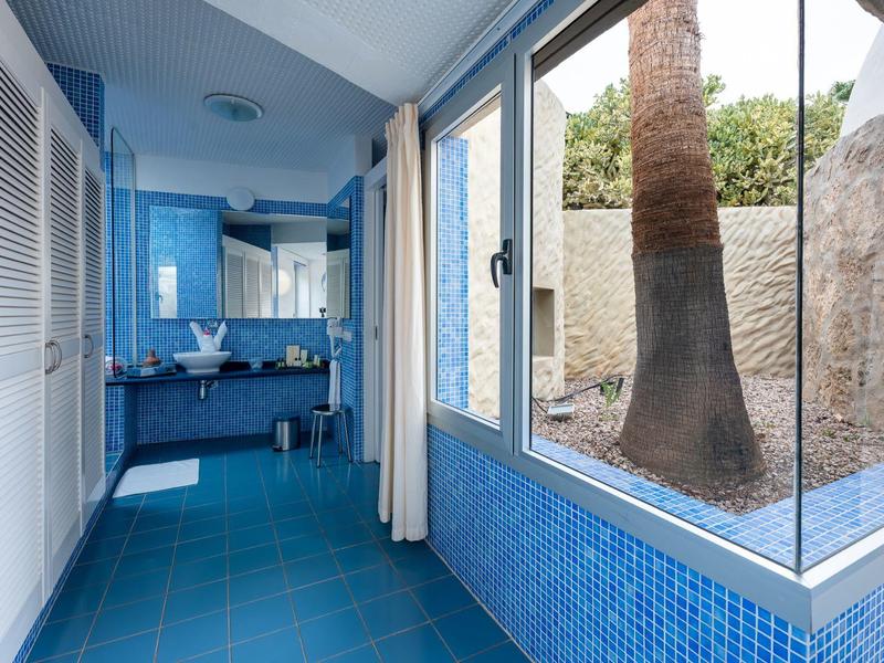 Flur mit blau gefliesten Wänden und Boden, Fenster mit Blick auf einen Baum und Waschbecken am Ende.