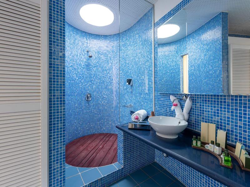Badezimmer mit blauen Mosaikfliesen, rundem Waschbecken und hölzernem Duschboden unter Tageslicht.