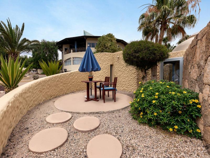 Gemütlicher Sitzbereich mit blauem Sonnenschirm und Pflanzen im Garten eines Hotels.