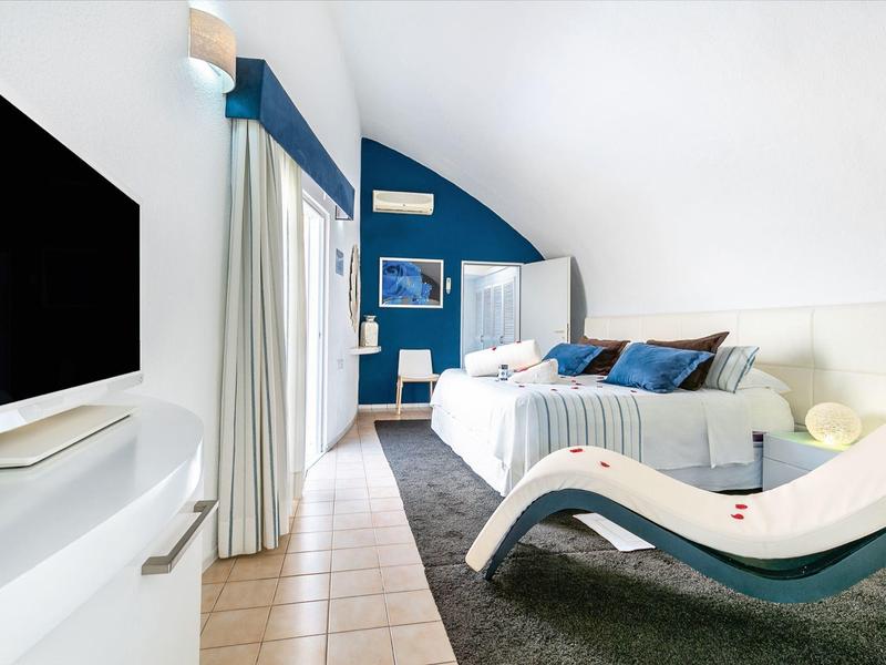 Modernes Hotelzimmer mit weiß-blauem Farbschema, gemütlichem Bett und Liegestuhl.