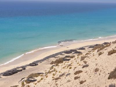 Karger Sandstrand mit vereinzelten Felsen und türkisem Meer unter klarem Himmel.