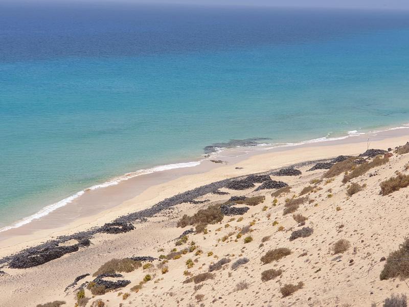 Karger Sandstrand mit vereinzelten Felsen und türkisem Meer unter klarem Himmel.