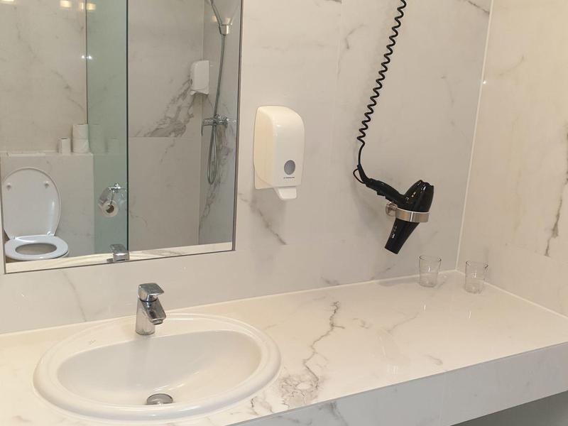 Hellweißes Badezimmer mit Spiegel, Handtrockner, Rundwaschbecken und offenem Unterschrank.