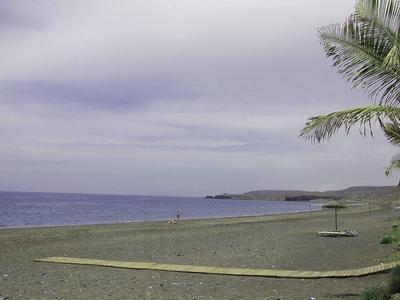 Leerer Sandstrand mit Palmen am rechten Rand und bewölktem Himmel über dem ruhigen Meer.