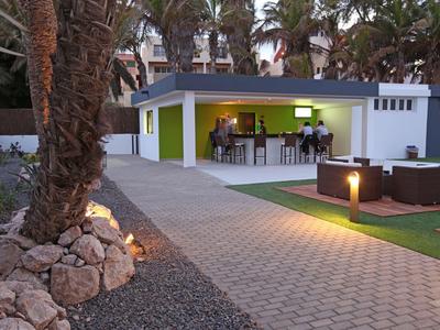 Moderner Gartenpavillon mit Bar, umgeben von Palmen und gepflastertem Weg bei Dämmerung.