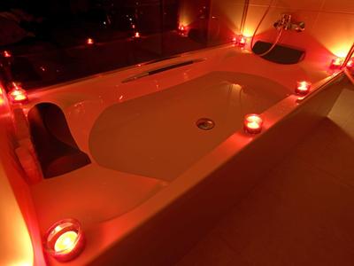 Weiße Badewanne mit Kerzenlicht, warmes rotes Licht, entspannende Atmosphäre, Badezimmerdetails.