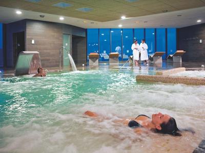Innen-Schwimmbad mit Whirlpool, Wasserfällen, mehreren Personen und großen Fenstern.