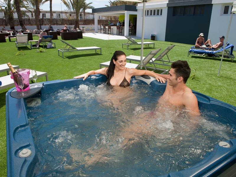 Twee mensen ontspannen in een buitenwhirlpool bij een hotel met uitzicht op zee.