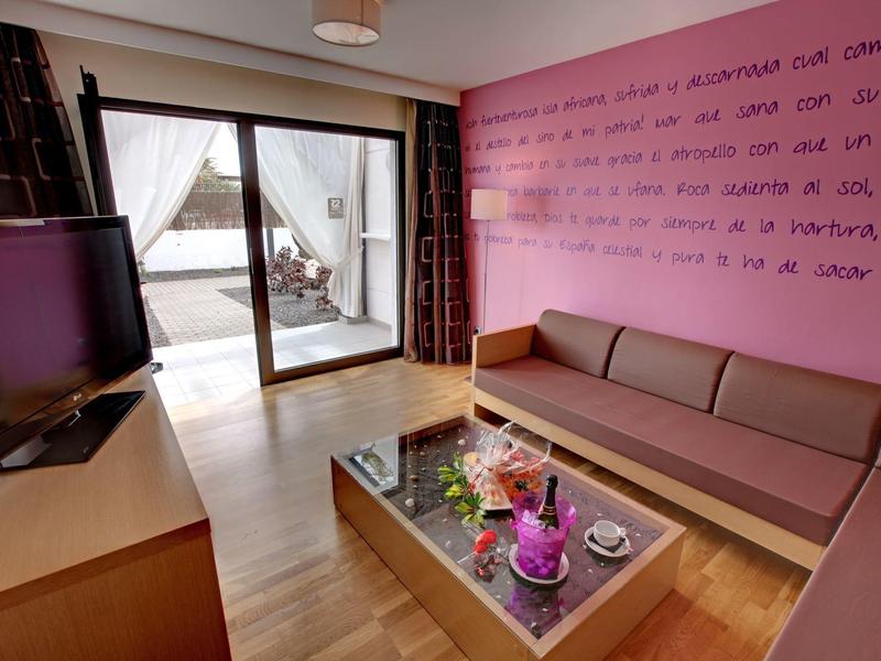 Moderne hotelkamer woonkamer met paarse muur, bank en glazen tafel met bloemen