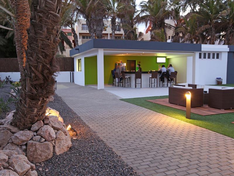 Modern buitengedeelte met bar en zitplaatsen, omgeven door palmbomen en verlichting.