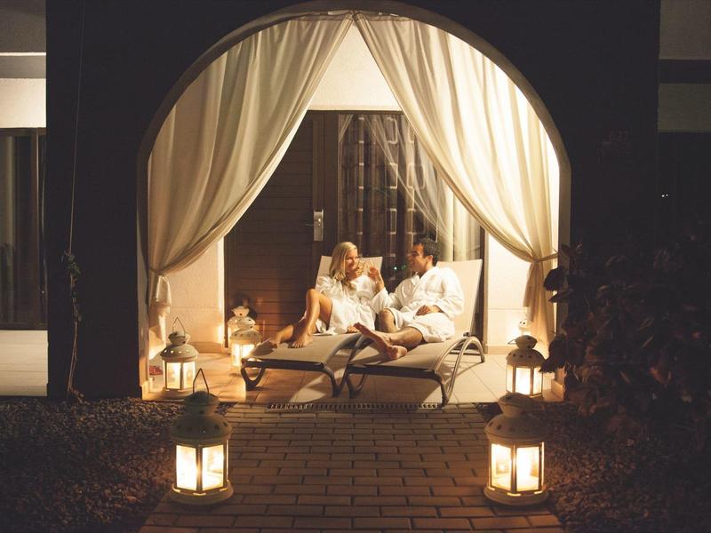 Koppel ontspant 's avonds op een luxe loungebank onder een overkapping met lantaarnlicht.