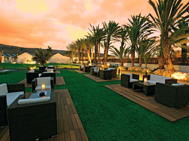 Luxe buitenlounge met moderne zitmeubels en palmbomen bij zonsondergang