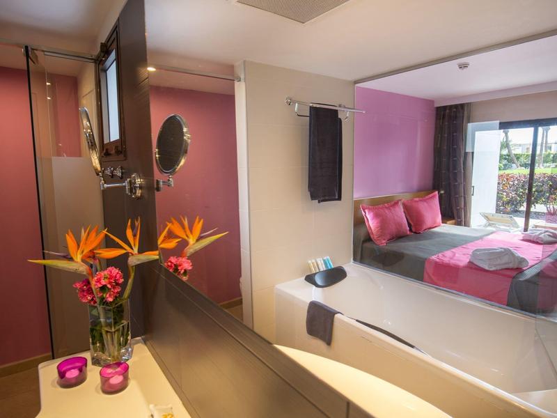 Hotelkamer met paarse accentmuur, bed met kussens en paradijsvogelbloemen in een vaas