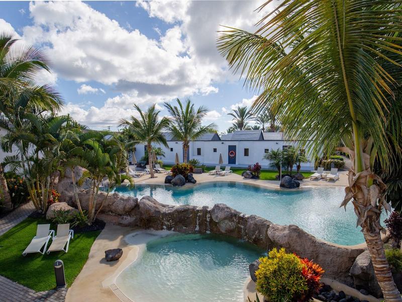 Hotelzwembad met tropische palmen en witte gebouwen onder blauwe lucht