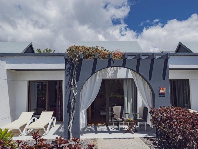 Moderne buitenterras met pergola, stoelen en ligstoelen voor wit gebouw.