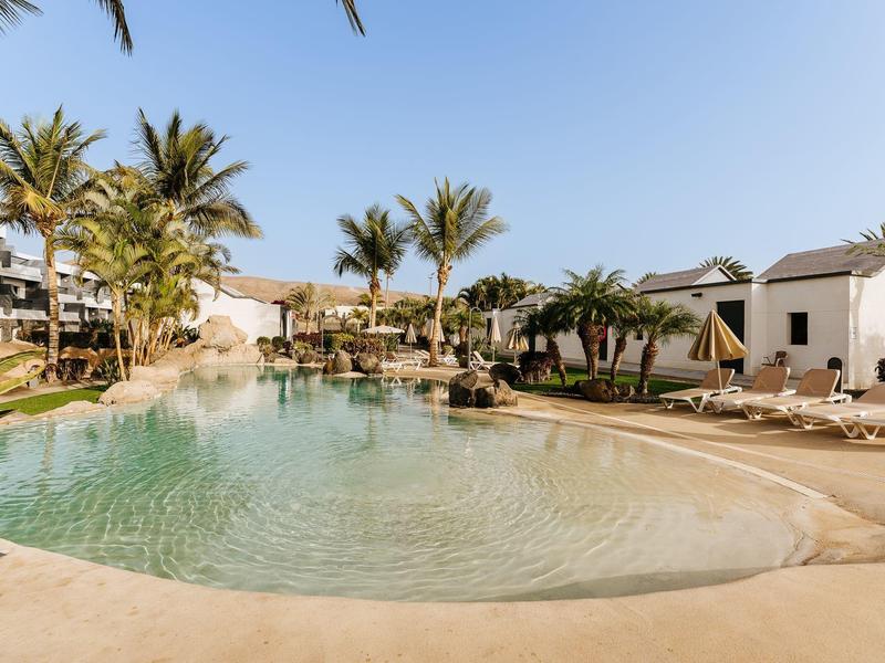 Zwembad met zonnige lucht, palmbomen en ligstoelen bij een hotelresort.