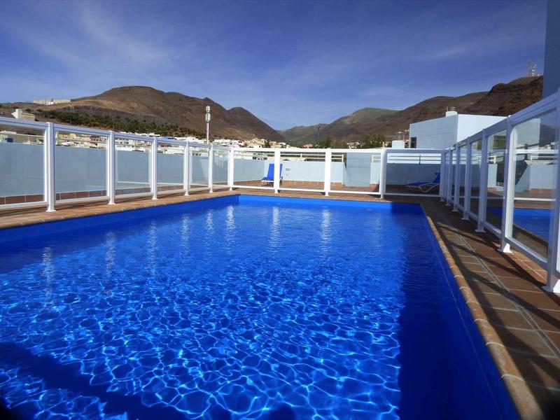 Outdoor-Pool mit klarem blauem Wasser, umgeben von weißem Geländer und Bergen im Hintergrund.