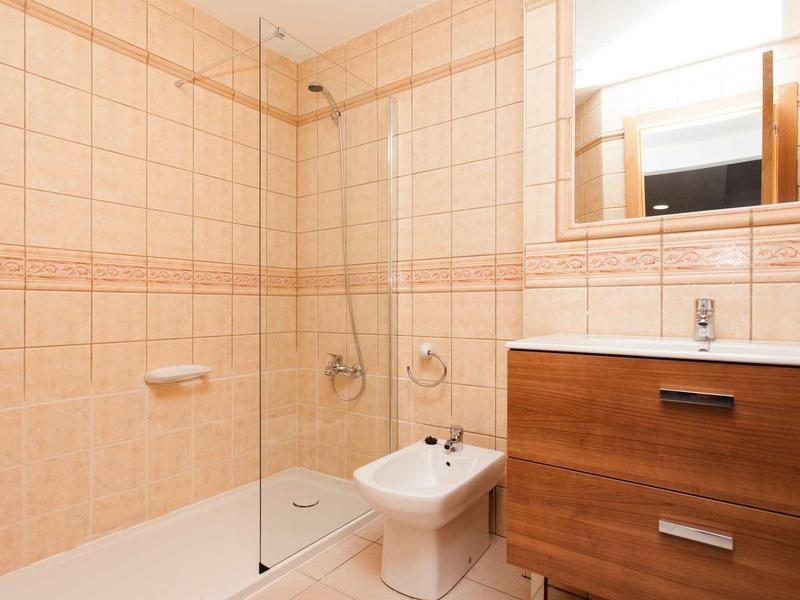 Helles Badezimmer mit beigen Fliesen, Glas-Duschabtrennung, Bidet und Holzwaschbeckenunterschrank.