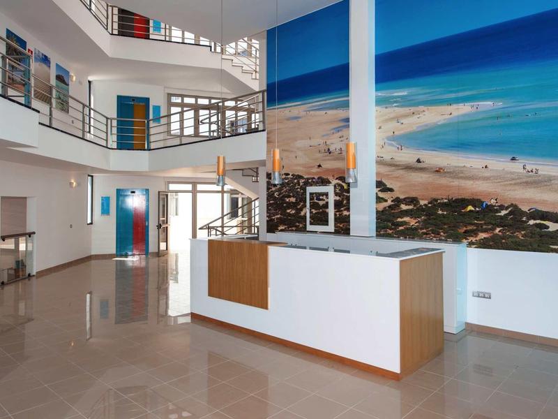 Heller Eingangsbereich mit blauem Wandbild, moderner Rezeption und Oberlichtfenstern.