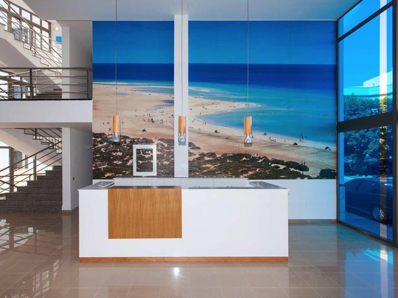 Moderner Eingangsbereich mit weißem Empfangstresen, großer Strandwandmalerei und Glasfront.