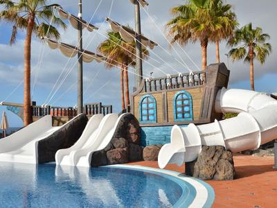 Wasserpark mit mehreren weißen Rutschen, Palmen und einem großen Schiff als Deko bei sonnigem Himmel.