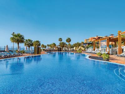 Großer Außenpool mit Palmen, Liegestühlen und klarem blauem Himmel in einem Resort.