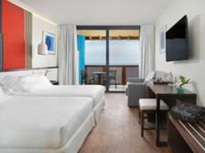 Helles Hotelzimmer mit Doppelbett, Flachbildschirm, Schreibtisch, Stuhl und Balkon mit Meerblick.