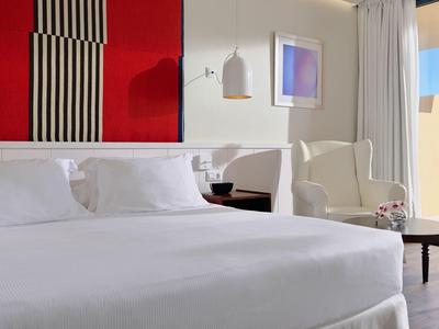 Modernes Hotelzimmer mit rundem Bett, weißer Bettwäsche und heller Einrichtung bei Tageslicht.