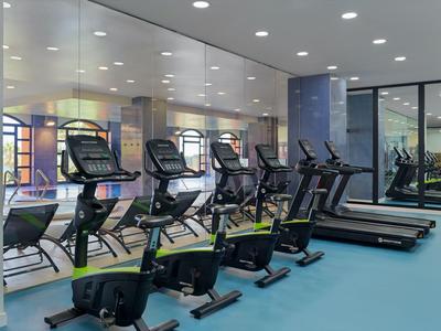 Moderner Fitnessraum mit Laufbändern und Fahrrädern, Spiegelwand reflektiert das helle Ambiente.