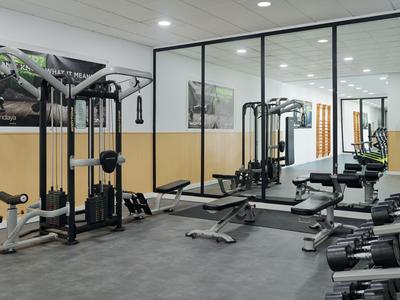 Moderner Fitnessraum mit Trainingsgeräten, Spiegelwand und Hanteln in einem Hotel.