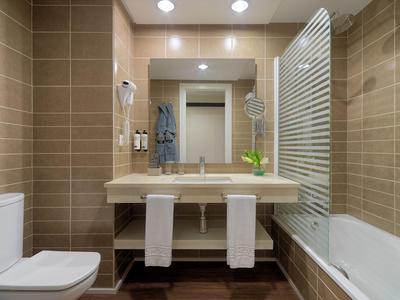 Modernes Badezimmer mit Waschbecken, Spiegel, Toilette und Badewanne mit Glasabtrennung.