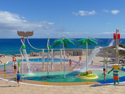 Bunter Wasserspielplatz mit Rutschen und Sonnenschirmen an einem Hotelpool am Meer.