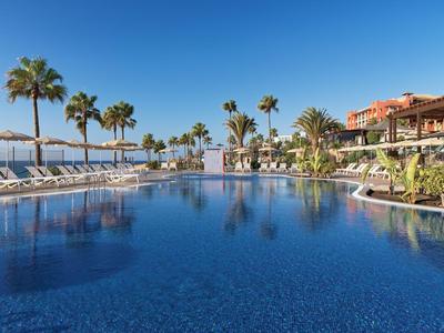 Großer Pool mit Liegestühlen und Palmen in einem sonnigen Hotelresort.