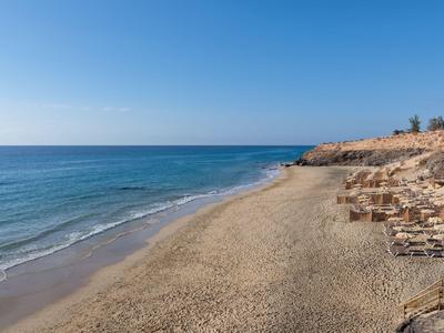 Weiter Sandstrand mit ruhigem Meer und Holzliegen unter klarem Himmel.