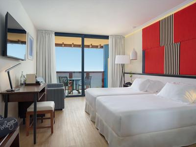Modernes Hotelzimmer mit Doppelbett, Schreibtisch, Fernseher und Balkon mit Meerblick.