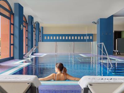 Frau entspannt im Hallenbad eines Hotels mit blauen Wänden und großen Fenstern.
