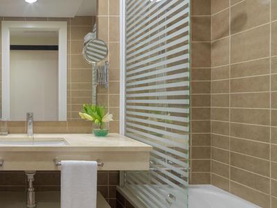 Modernes Badezimmer mit Waschbecken, Spiegel und Badewanne, beige geflieste Wände und Glas-Duschwand.
