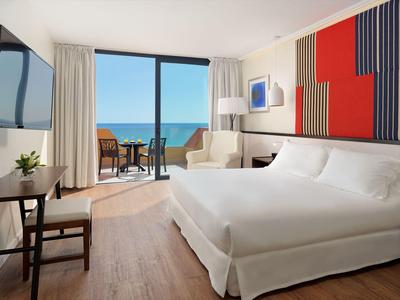 Helles Hotelzimmer mit Doppelbett, Balkon und Meerblick, modern eingerichtet.