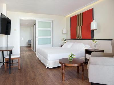 Modernes Hotelzimmer mit Doppelbett, beigem Sofa, Holzboden und minimalistischer Einrichtung.