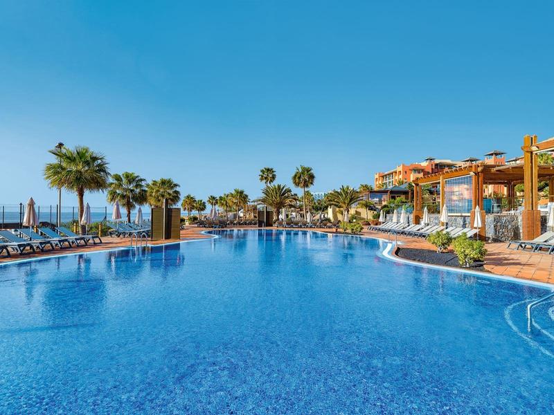 Großer Außenpool mit Palmen, Liegestühlen und klarem blauem Himmel in einem Resort.