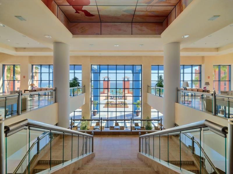 Helles, modernes Treppenhaus mit Glasgeländern, Säulen und großen Fenstern mit Blick nach draußen.