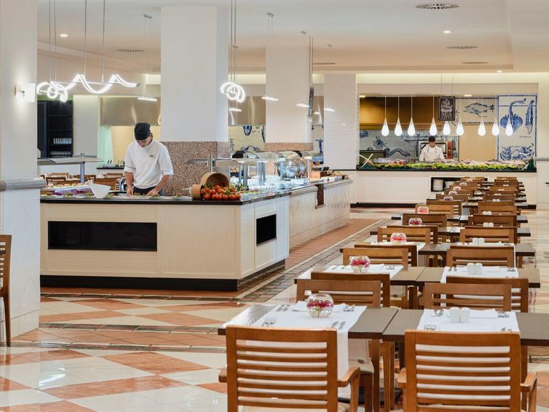 Hell beleuchteter, moderner Speisesaal mit holzfarbenen Stühlen und beigem Marmorboden.