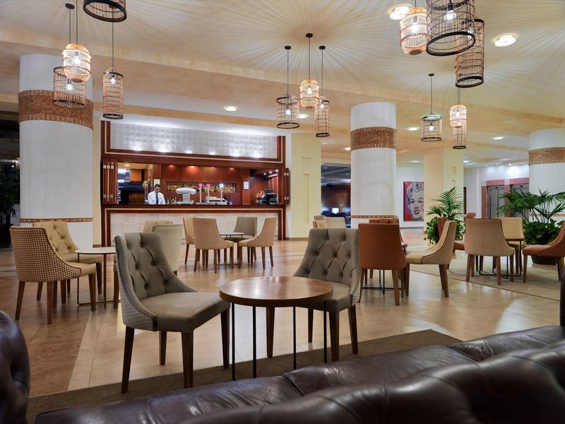 Moderner, heller Gastraum mit Holzboden, runden Tischen, Polsterstühlen und Deckenlampen.